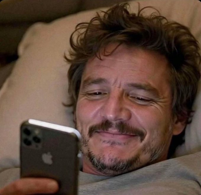 A man lies in bed smiling warmly as he looks at his iPhone, perfectly capturing the relaxed "gm" (good morning) vibe of the post celebrating the Base ecosystem's community-driven success and inclusive growth.