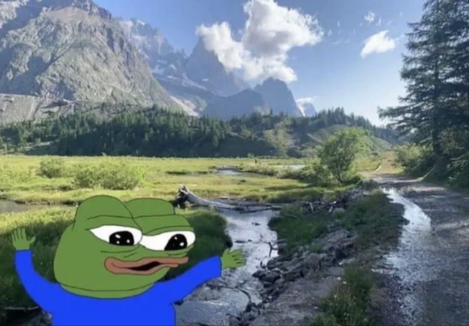 A Pepe the Frog meme character with his arms raised stands in the foreground of a scenic mountain landscape featuring a stream, green meadow, and snow-capped peaks.