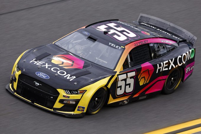 A NASCAR race car (number 55) in a black, yellow, and pink HEX.com livery racing on a track.