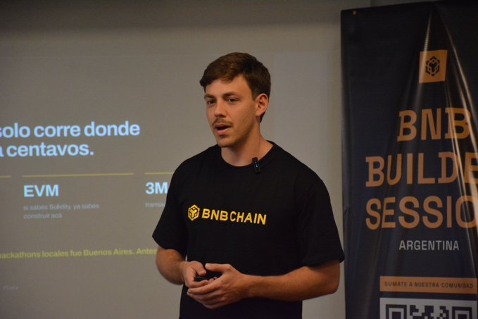 A man stands presenting at a BNB Builders Session in Argentina, wearing a black BNB Chain t-shirt, with a presentation slide visible behind him.