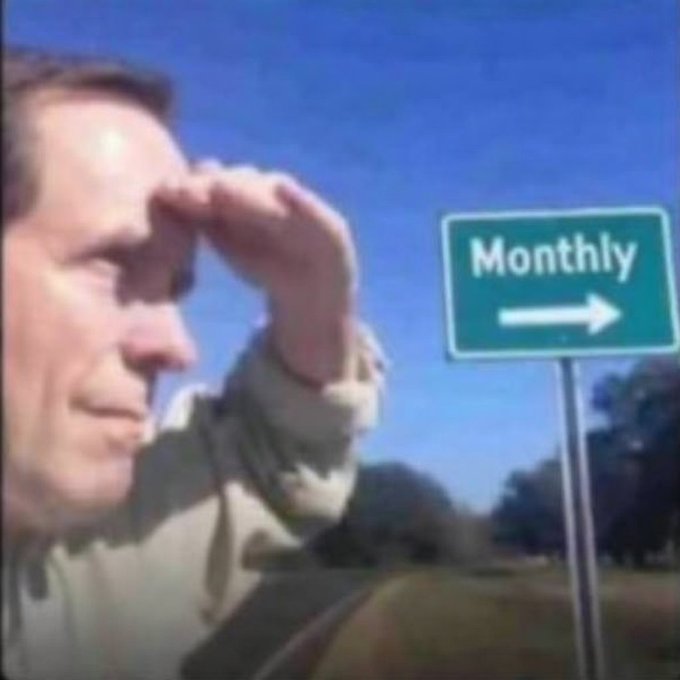 A man shields his eyes as he looks towards a road sign that reads "Monthly" with an arrow pointing to the right, mirroring the post's question about "monthly @Stake".