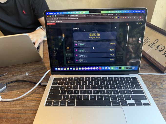 A laptop on a wooden desk displays a browser with a cryptocurrency wallet interface showing a balance of $335.50 VALOR, with a person partially visible in the background.
