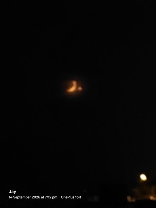 A nighttime photo shows a glowing crescent-shaped object, possibly the moon, in a dark sky, timestamped 14 September 2026 at 7:12 pm, taken with a OnePlus 13R.