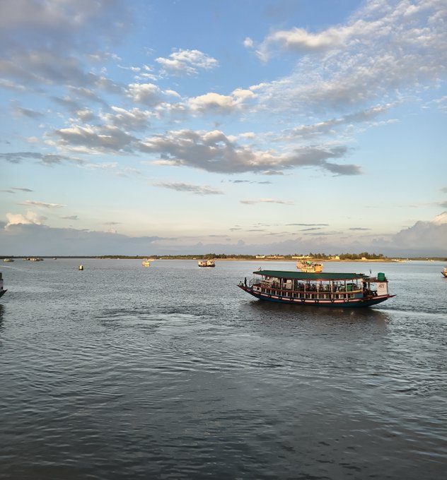 A scenic view of traditional wooden boats floating on calm waters under a partly cloudy sky at sunset.