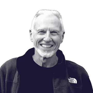 Black and white portrait of a smiling older man with a gray beard wearing a The North Face fleece jacket.