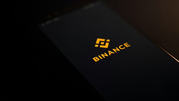 A smartphone displays the orange Binance cryptocurrency exchange logo against a dark background in low lighting.