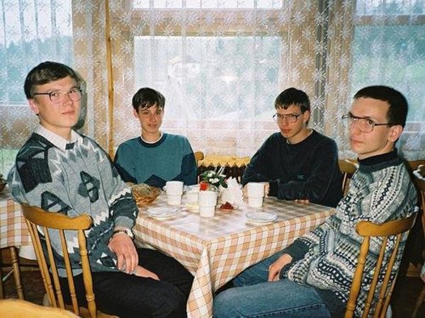 Four men in casual sweaters sit around a checkered tablecloth having what appears to be breakfast together, with a small flower vase and coffee cups on the table, illustrating a relaxed morning gathering that the post humorously frames as a ritual of reading whitepapers with cryptocurrency influencers @bull_bnb, @Spigg1115, and @BenTodar.