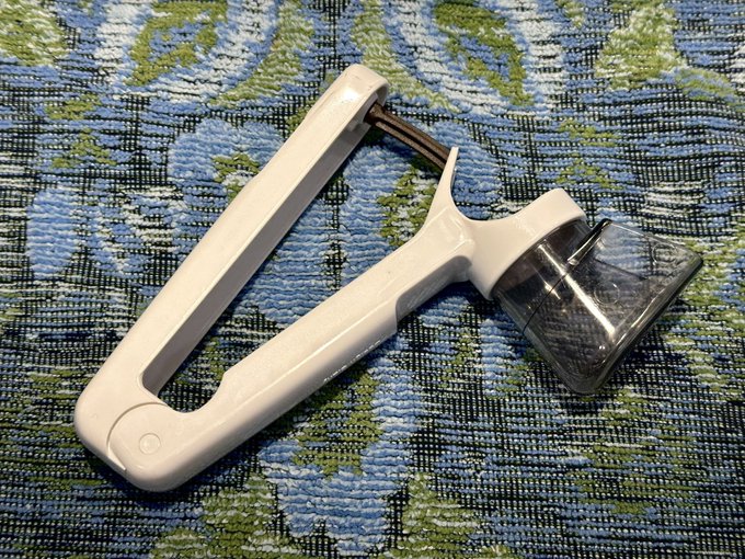 A white and chrome handheld citrus juicer rests on a blue, green, and white floral patterned woven fabric.