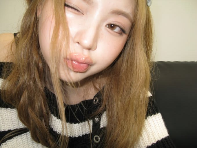 A young woman with long light brown hair winks at the camera while puckering her lips in a kiss expression. She is wearing a black and white striped knit top and appears to be taking a close-up selfie indoors.