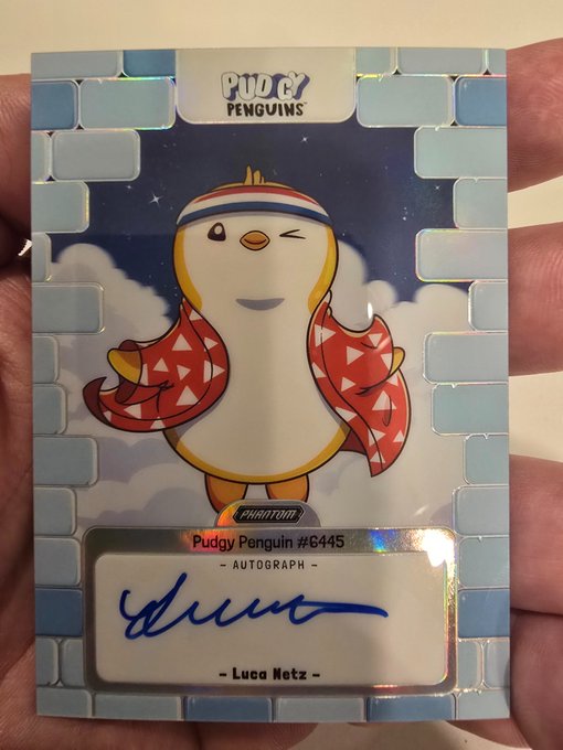 A holographic 'Pudgy Penguins' trading card (#6445) featuring a penguin in a red patterned scarf, with an autograph signed by 'Luca Netz' on the autograph panel.