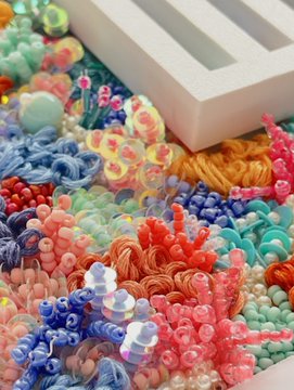 The image features a close-up of a white box with a unique design on its side, surrounded by an array of colorful beads and sequins. The beads are scattered all over the box's surface, creating a vibrant and eye-catching display. In addition to the box, there is also a small piece of paper placed near it.