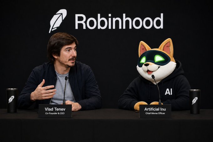 The image shows a humorous staged press conference with a Robinhood logo backdrop, featuring Vlad Tenev (Co-Founder & CEO) seated next to a person in a fox/cat mascot costume wearing a green visor labeled "AI" with a nameplate reading "Artificial Inu, Chief Meme Officer." This visual gag satirizes the Robinhood co-founder "hiring" a meme token as a corporate officer, playing directly on the post's enthusiasm for a $AI position and Robinhood's recent listing of the meme coin.