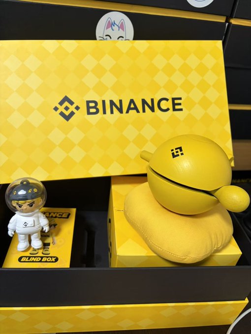 The image features a small toy astronaut figurine sitting next to a yellow bin box with "Binance" written on it, as well as a yellow ball and a pillow. The toys are placed together, creating an interesting scene that could be related to the post about Binance.