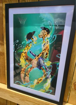 A framed vibrant artwork features giraffes wearing pirate hats and chains intertwined with a central skull and floral elements against a green and orange background.
