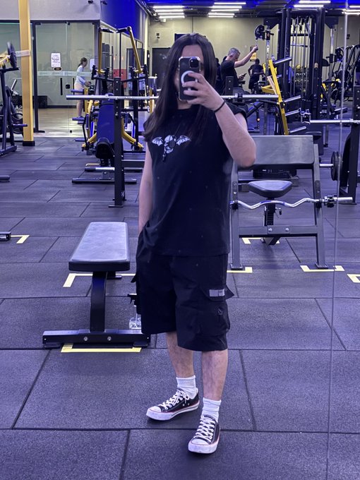 A person takes a mirror selfie in a gym wearing black shorts, a black graphic tee, and Converse sneakers, capturing a moment of fitness focused on personal health. The image visually represents the post's message about stepping away from screens (including crypto platforms like Uniswap and TradePools) to prioritize physical well-being.