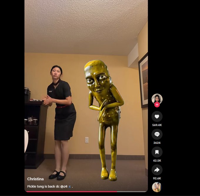 A TikTok video screenshot showing a woman named Christina standing next to a green 3D pickle character in an office, with the caption 'Pickle tung is back dc @J4'.