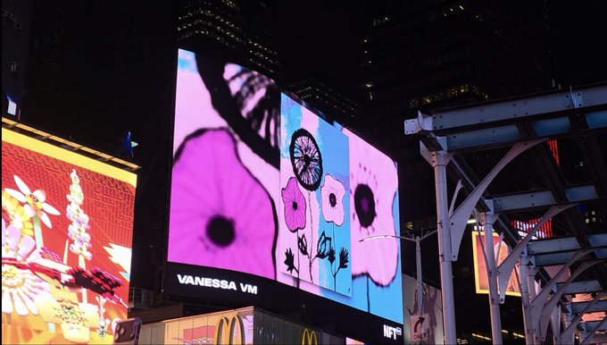 An illuminated nighttime billboard in an urban setting displays artwork of pink poppies by 'VANESSA VM' with a McDonald's logo visible below.