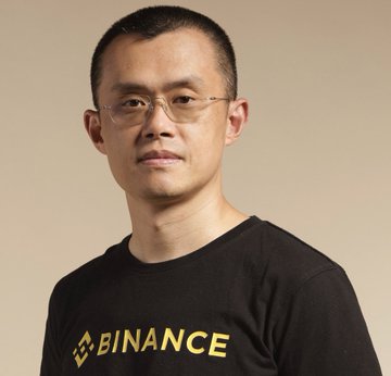 A man wearing a black Binance t-shirt and glasses poses against a beige background. The image relates to the post as it features Changpeng Zhao (CZ), Binance's former CEO, discussing the EU's MiCA licensing challenges affecting the exchange's European users.
