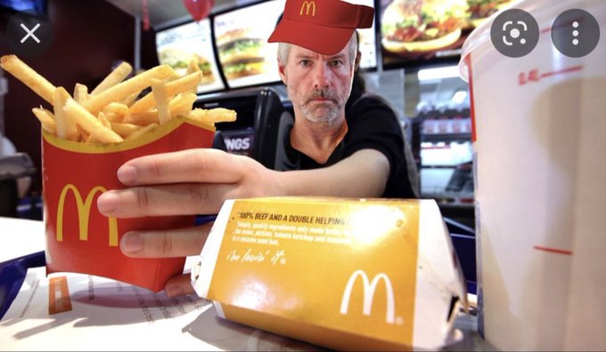 A man wearing a red McDonald's cap behind a counter reaching toward the camera, with a carton of French fries and a Double hamburger box in the foreground.