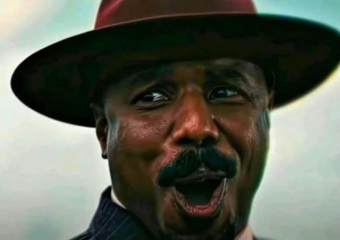 A close-up photograph captures a man wearing a dark red wide-brimmed hat, smiling broadly with an exaggerated expression.