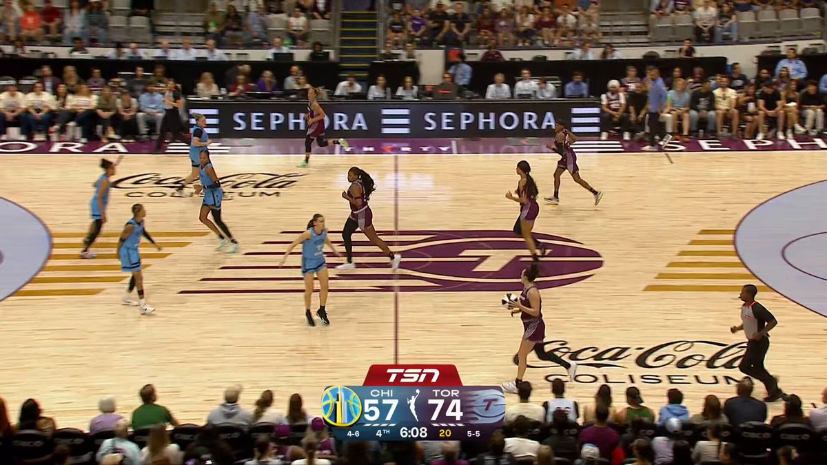 The image shows a basketball game taking place, with players actively participating on an indoor court. The crowd of spectators can be seen watching from various positions around the court. A scoreboard is visible above the court displaying the score of the game as "73-76". The image also includes text that reads "The highlight reel was jumpin' last night Check out the top plays from Sunday's Comm Cup action! #WNBASeason30 | @coinbase". This suggests that a special event or highlight moment in the basketball game has captured the attention of both players and spectators.