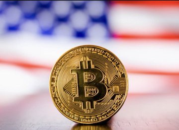 A physical Bitcoin token displayed in front of an American flag background.