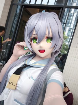 A cosplayer dressed as the anime character Hoshimachi Suisei with green eyes poses for a photo, wearing a white outfit with teal accents.