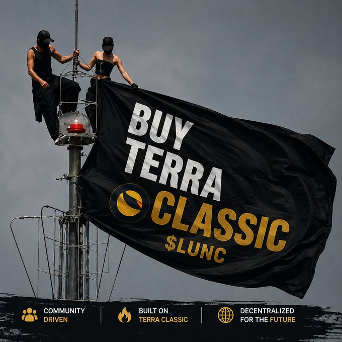 Two masked individuals in black attire stand atop a high metal pole, unfurling a large black flag that reads "BUY TERRA CLASSIC $LUNC" alongside the project's logo, visually reinforcing the "Buy the Dip $LUNC" message with a dramatic, rebellious promotional image highlighting community-driven, decentralized crypto advocacy.