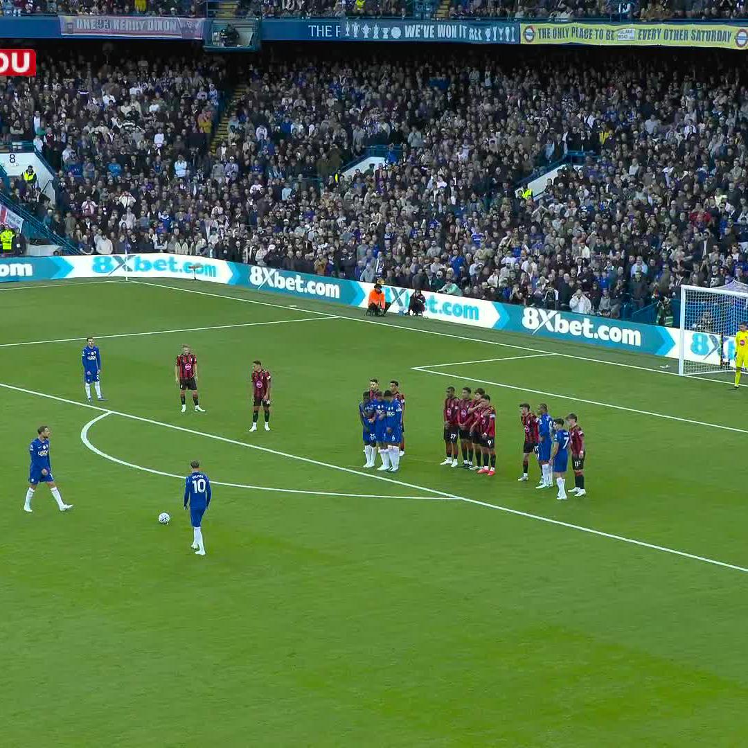 A football match scene at Stamford Bridge shows Chelsea players (in blue) preparing for a free kick against Bournemouth (in red), with advertising boards reading "8Xbet.com" and a stadium banner declaring "THE ONLY PLACE TO BE EVERY OTHER SATURDAY" visible in the stands. The image captures the set-piece setup, likely the moment before Jordan Henderson's stunning goal mentioned in the caption.
