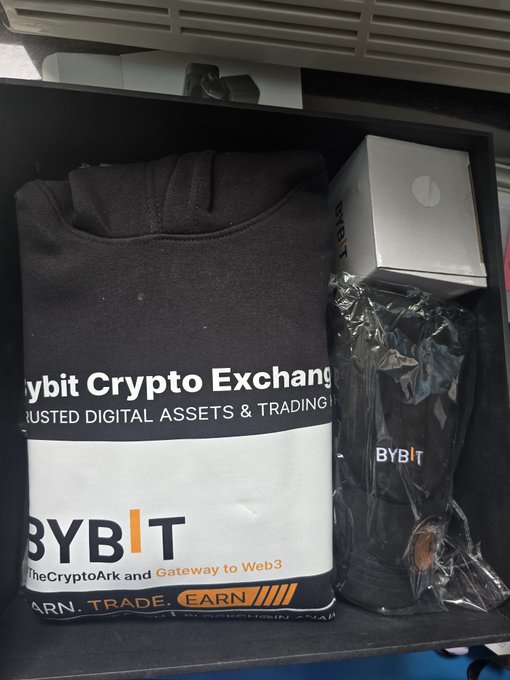 A black box containing Bybit Crypto Exchange merchandise, including a branded sweatshirt and what appears to be a tumbler wrapped in plastic.