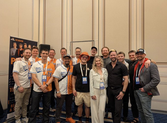 A group of around 14 people pose together indoors, several wearing white and orange "BTC Sessions" baseball jerseys with numbers like "26," alongside a partial banner reading "BTC INNOVATION" and "It takes A Re..."—likely capturing the team after a Bitcoin conference event. The caption fits the speaker's farewell to the @btcsessions channel, marking their departure from the team they helped grow.