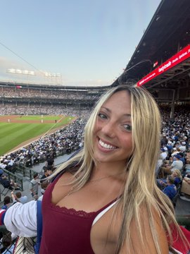 A blonde woman smiles while taking a selfie at a packed baseball stadium, with a full crowd visible in the background under a clear blue sky. The caption aligns with her promoting her Polymarket promo code "BREE" for $20 off while cheering on her "Cubbies" (Chicago Cubs) to win.