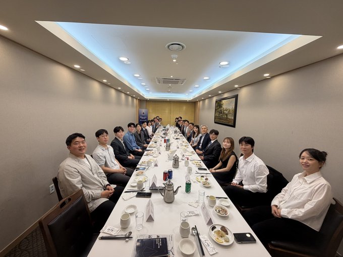 A group of approximately 20 people sit around a long rectangular table in a well-lit conference room during a formal meeting, with white table settings, water bottles, and documents arranged in front of them. The image captures the Ethereum Korea Policy Roundtable gathering, showing attendees from the Ethereum Foundation, Optimism, and Korean financial and legal institutions engaged in discussion.