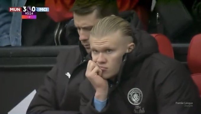 A Manchester City football player with blonde hair sitting on the bench in a puma jacket, looking pensive during a Premier League match (MUN 3-0 MCI, 93:14).