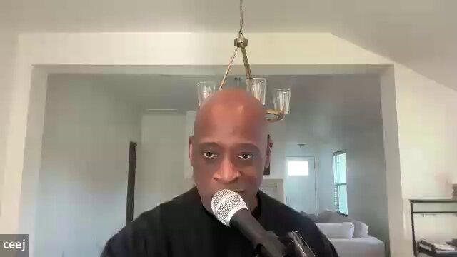 The image shows a man wearing a black shirt holding a microphone with a gold chain hanging from it. The background features a white wall and a window. The caption reads "XRP was called the banker coin for years. Now everyone wants to be the banker coin. That tells you a lot about where this market is headed. What changed: XRP, or the rest of the industry?". This suggests that the man with the microphone might be discussing the rise and fall of cryptocurrency XRP in relation to the banking industry. The image could also be interpreted as an advertisement for XRP, highlighting its potential impact on the financial world.