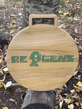 A round wooden plaque or sign engraved with the word 'REGENT' sitting on a wooden surface outdoors, with fallen leaves visible in the background.