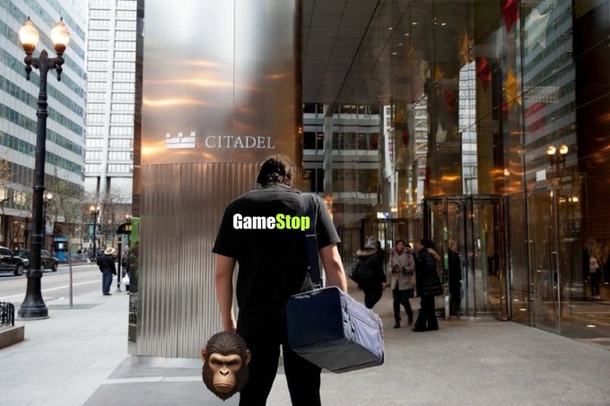 A man wearing a "GameStop" shirt walks toward the Citadel building carrying a duffel bag and a chimpanzee mask, symbolizing the retail-versus-institutional battle behind the $GME memecoin narrative that bridges crypto and Wall Street.