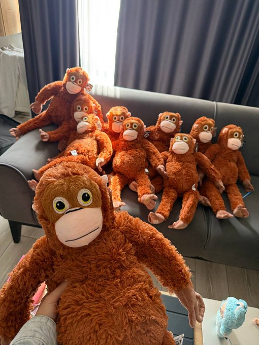 The image features a large group of stuffed animals, including several teddy bears and an orange monkey plushie, sitting together on a couch. A person's hand can be seen holding one of the stuffed animals, possibly posing for a photo or just enjoying their company. The stuffed animals are arranged in various positions, creating a cozy and inviting atmosphere. The post "Time to spread the love" suggests that sharing this image with others could bring joy and warmth to those who see it, encouraging them to spread positivity and love through simple acts of kindness.