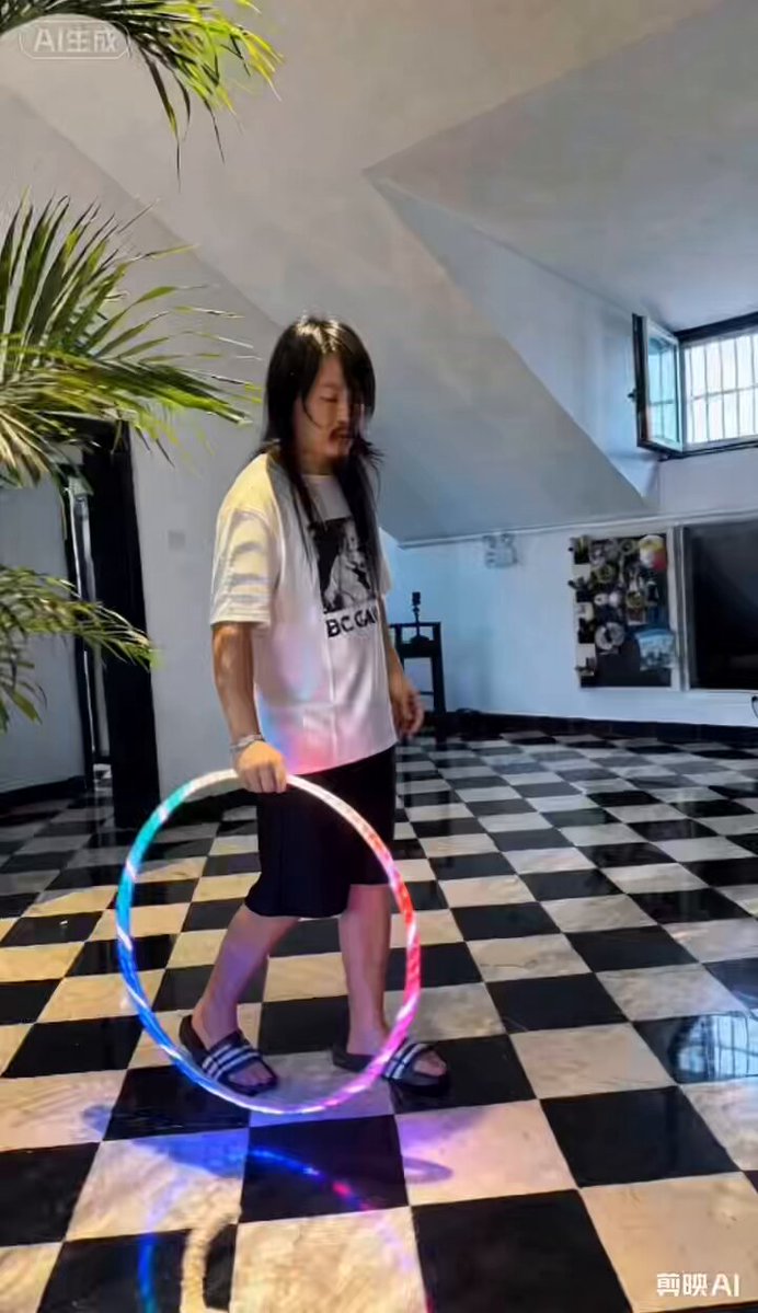 The image features a woman wearing a white shirt, black shorts, and slippers while holding a hula hoop with colorful lights inside of her hand. The background shows a checkered floor and a potted plant, creating an indoor setting for this activity. There is also text in the image that reads "那些说OKB 到60u抄底的兄弟们", which translates to "okb" being used as a greeting or a nickname by someone else.