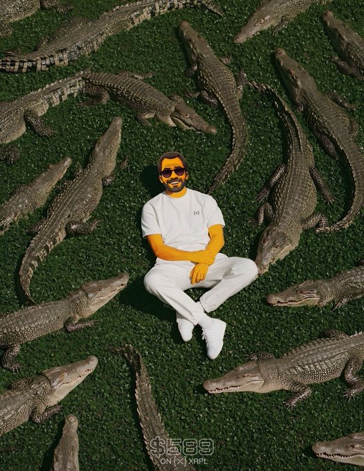 An aerial shot of a man in white clothing and sunglasses sitting cross-legged on grass surrounded by a circle of crocodiles, with a '$5500 ON XRP' caption at the bottom.