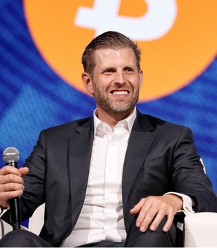 Eric Trump smiles while seated on stage at what appears to be a panel discussion, holding a microphone, in connection with his comments about a booming sector sparking "massive" growth in crypto.
