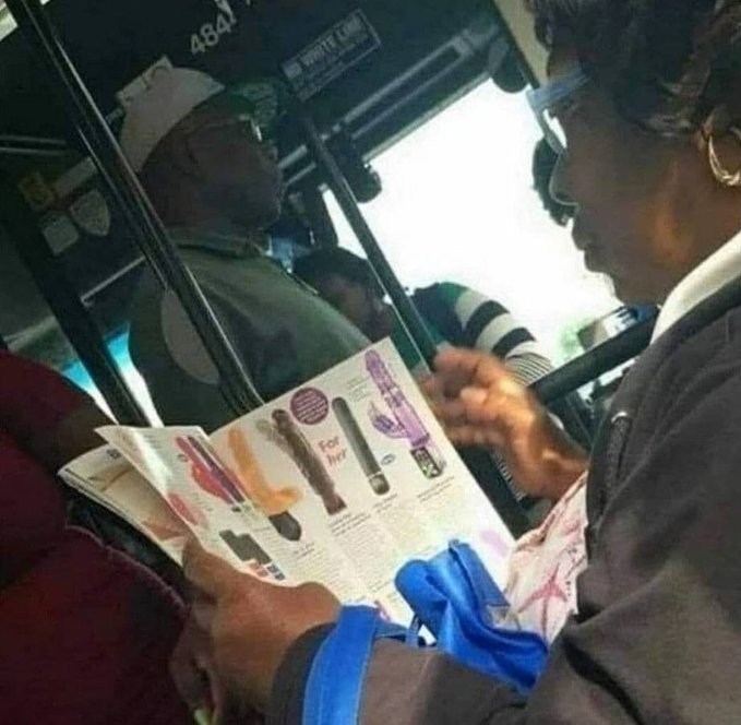 A candid photo taken on a public bus showing a man reading a catalog of adult products featuring various vibrators, with other passengers visible in the background.