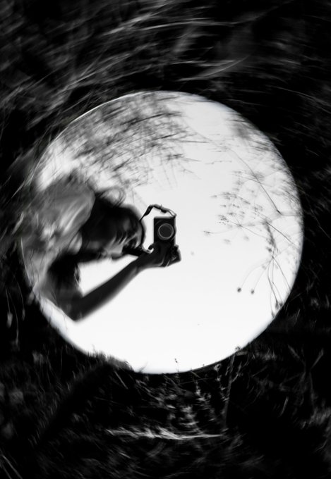 A high-contrast black and white silhouette shows a person holding a camera against a large, bright full moon.