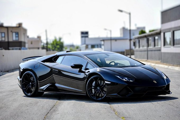 A sleek black Lamborghini Huracán parked on an urban street, showcasing its aggressive styling, sharp angular design, and black alloy wheels.