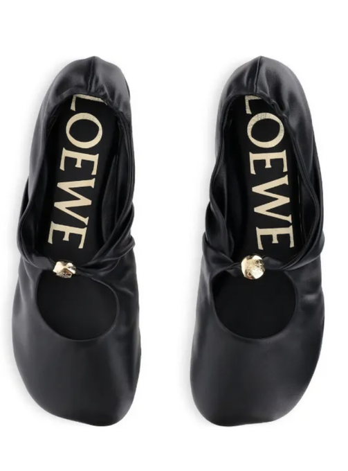 A pair of black LOEWE leather ballet flats displayed against a white background, featuring the brand's gold logo in the insole and a knotted strap with a gold metal detail on the toe.