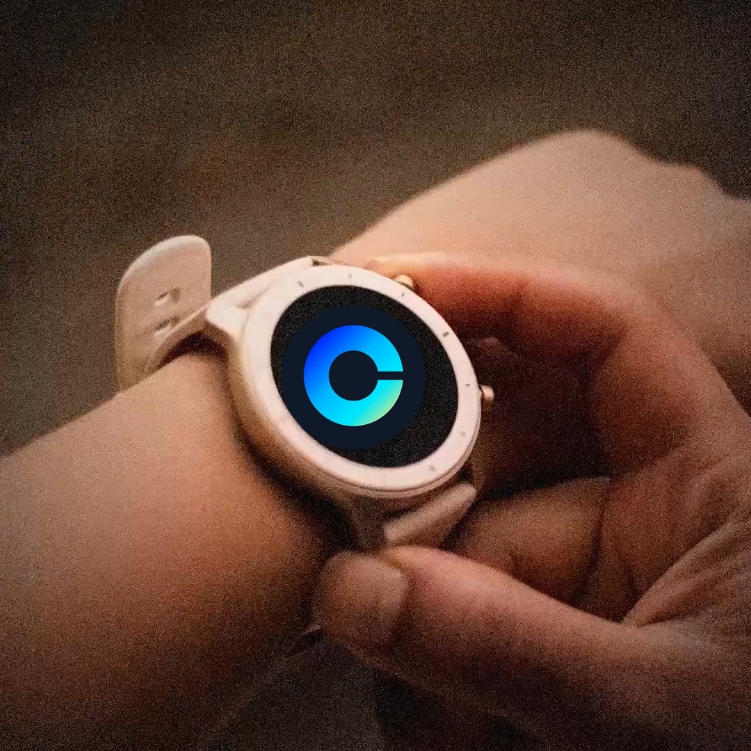 A close-up photo of a person's wrist wearing a white smartwatch with a glowing blue circular logo on the screen.