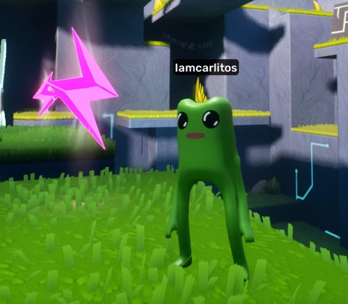 A green frog-like avatar character named '!amcarlitos' standing in a grassy 3D game environment next to a glowing pink origami star.