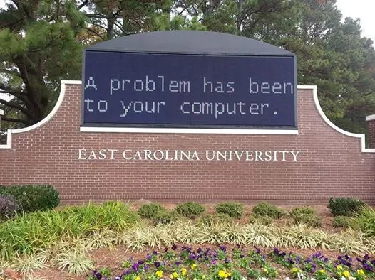 The brick entrance sign for East Carolina University displays the blue screen of death error message: 'A problem has been to your computer.'