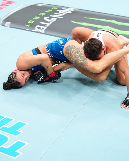 A UFC fighter secures an armbar submission on the mat, with "MONSTER ENERGY" branding visible on the canvas and "UFC" on the fighter's shorts. The image captures the winning moment of Casey King's victory over Eduarda Moura as referenced in the post.