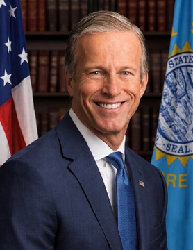 A man in a dark blue suit with a blue tie smiles in front of an American flag and a "STATE" seal flag, appearing to be an official government portrait. The accompanying post about the CLARITY Act suggests he may be a U.S. Senator connected to the legislation.